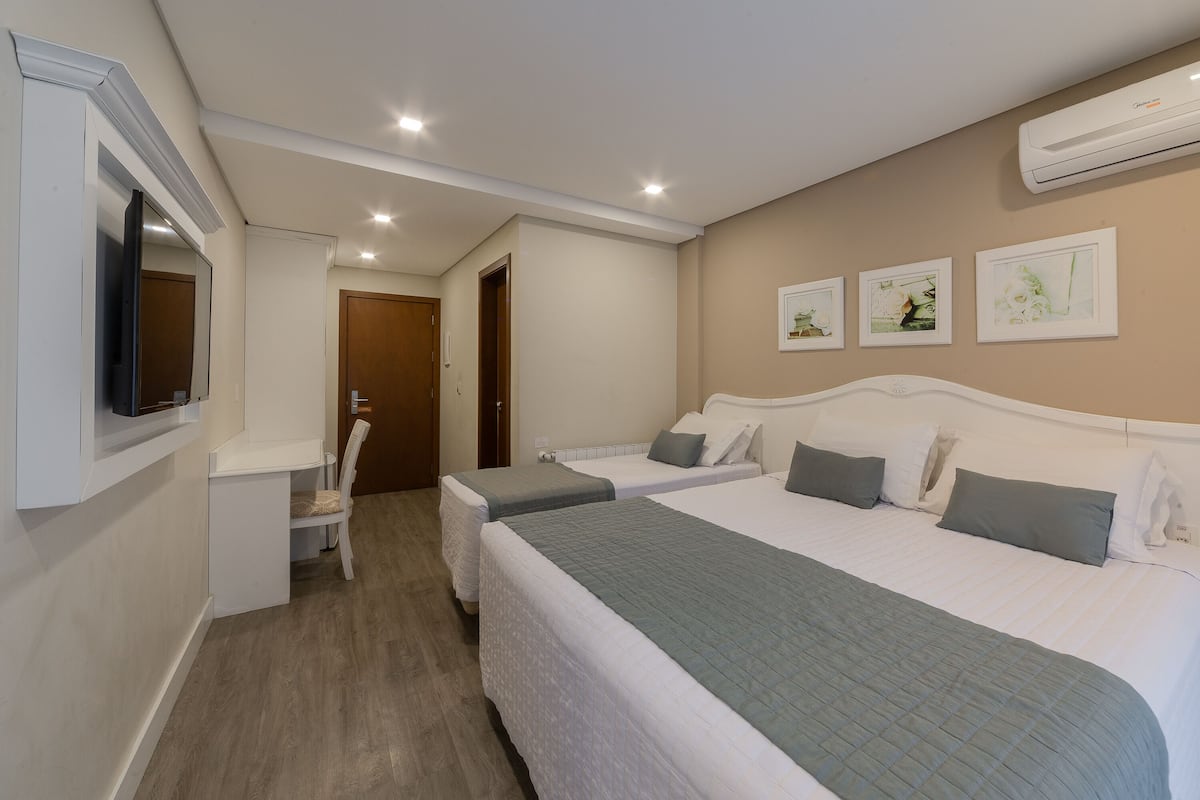 A hotel room with two beds, a desk, a chair, and a TV.