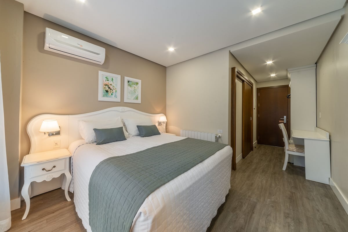 A bedroom with a bed, bedside table, lamp, and an air conditioning unit on the wall.