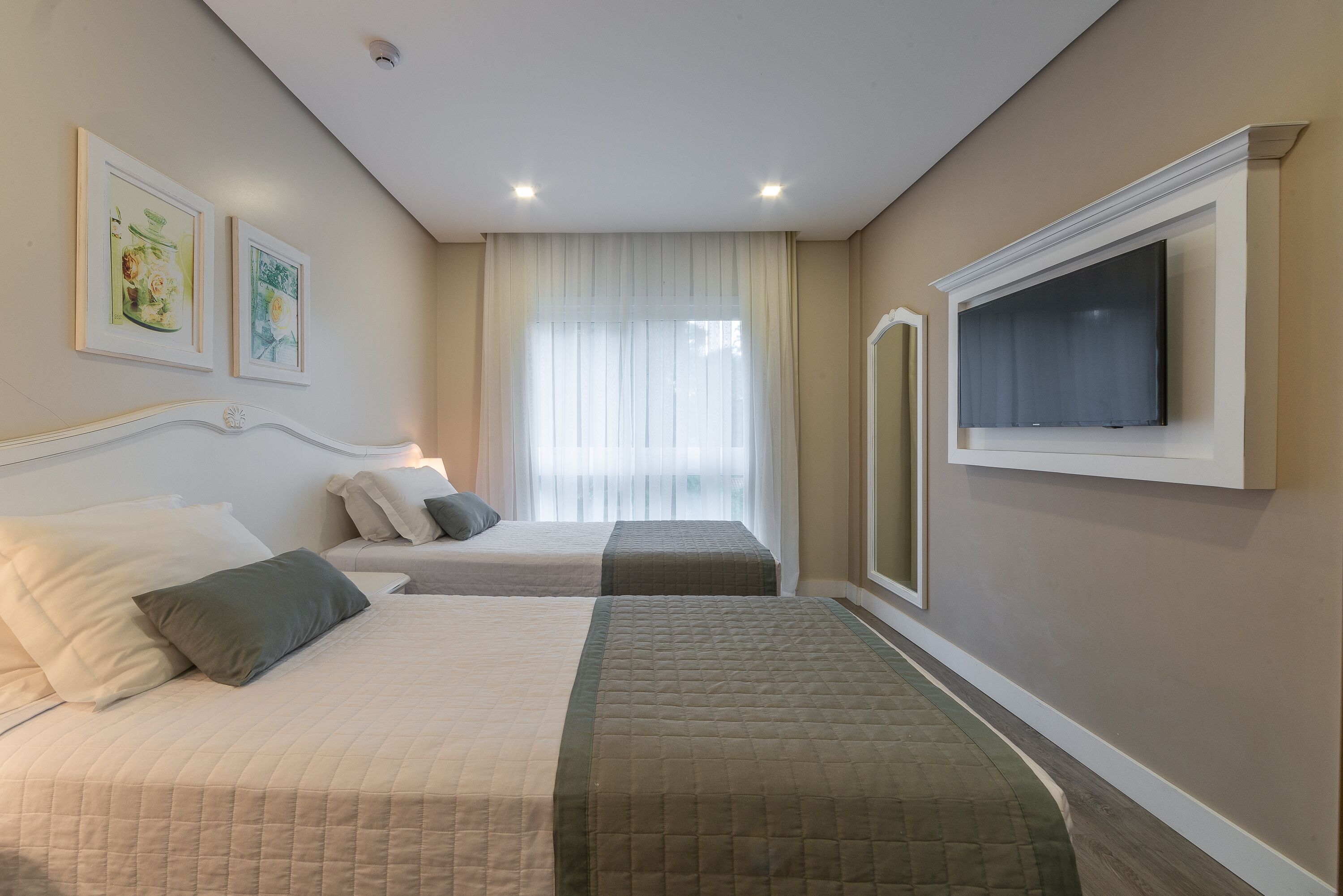 Habitación de hotel con dos camas, un televisor de pantalla plana montado en la pared y obras de arte en la pared.