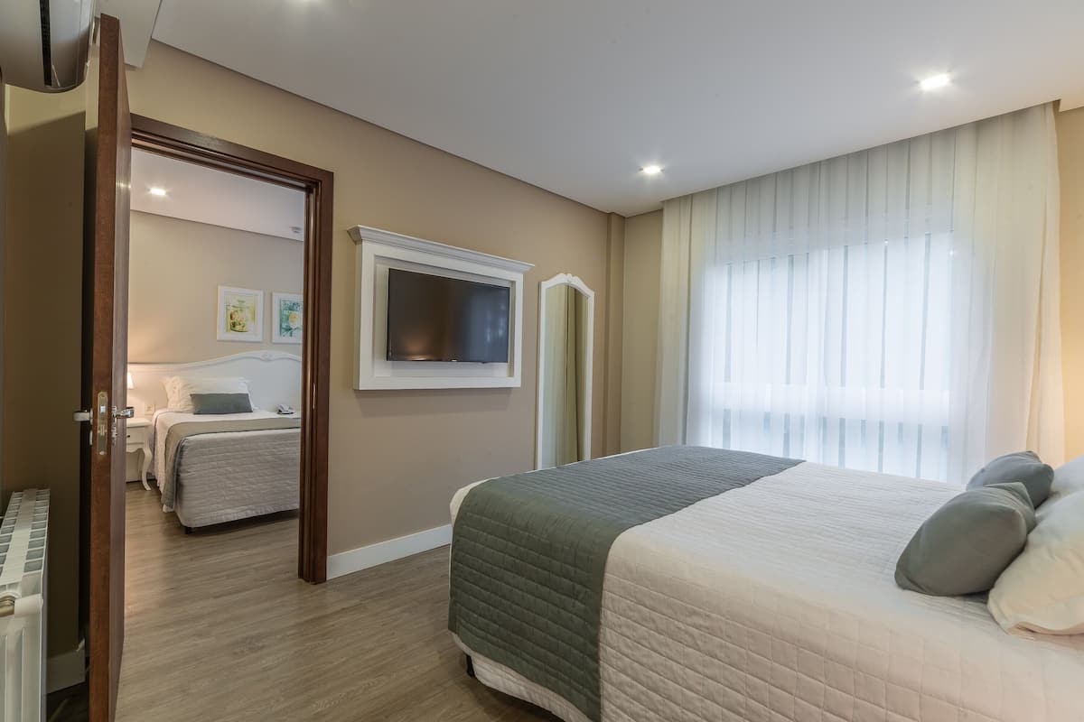 A hotel room with a bed, a television, a mirror, and a door leading to another room.