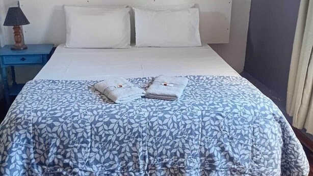 A bed with a patterned bedspread, a nightstand with a lamp, a framed picture on the wall, and a wall-mounted air conditioner. - Roma Hotel (Porto Alegre)