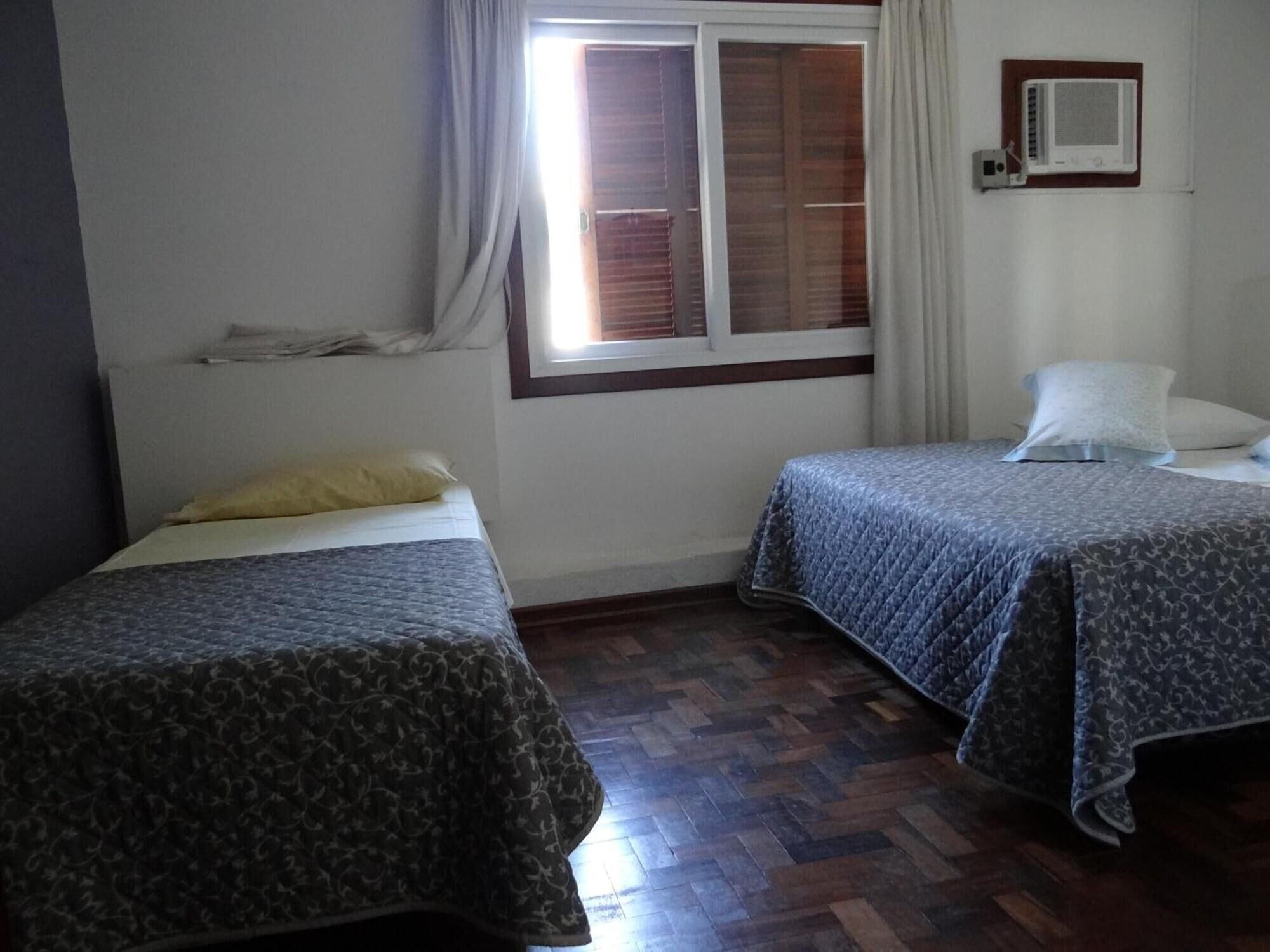 Habitació amb dos llits, una finestra amb persianes, un calefactor penjat a la paret i un sòl de fusta.