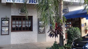 A hotel named 'ROMA HOTEL' with a tiled facade, a large window with lace curtains, and a palm tree in front. - Roma Hotel (Porto Alegre)