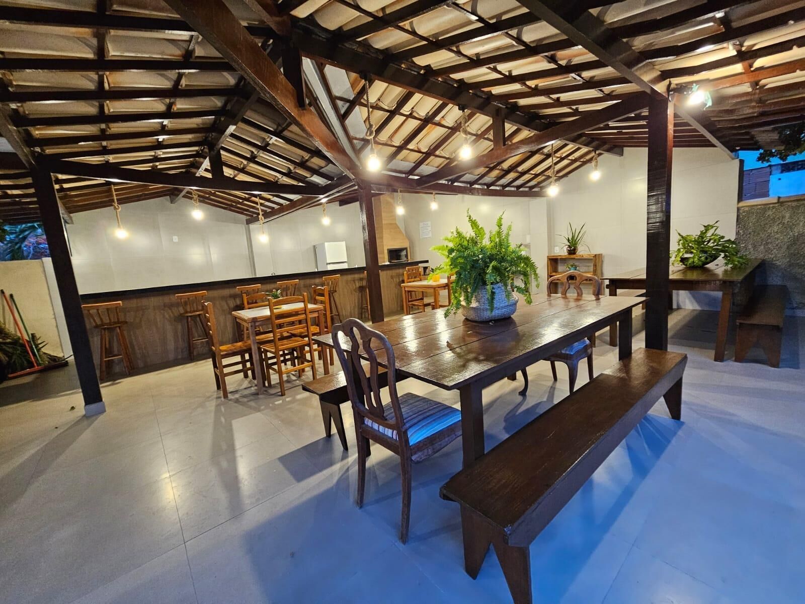 Un comedor interior con techo alto, mesas y sillas de madera, y plantas en macetas.