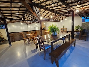 An indoor dining area with a high ceiling, wooden tables and chairs, and potted plants. - Pousada Recanto das Emerências (ARMACAO DOS BUZIOS)
