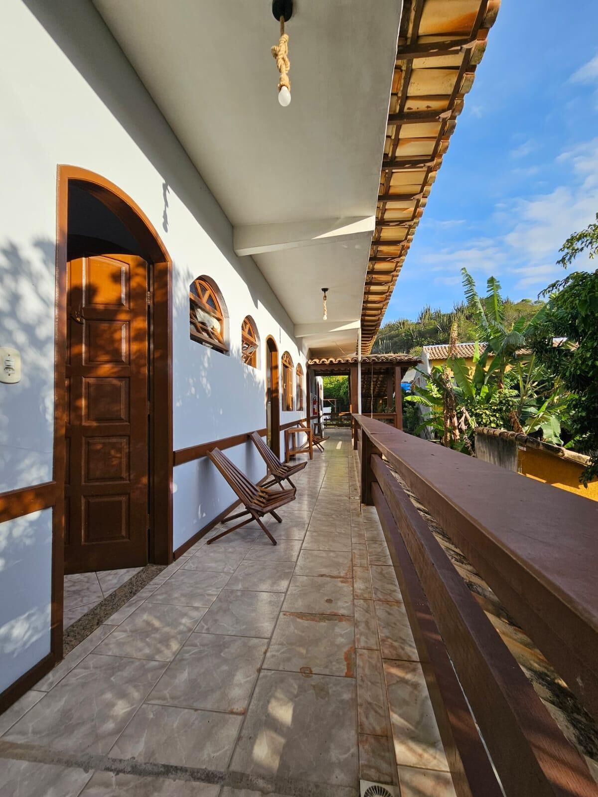 A covered outdoor area with a tiled floor, wooden benches, and a railing overlooking a garden.