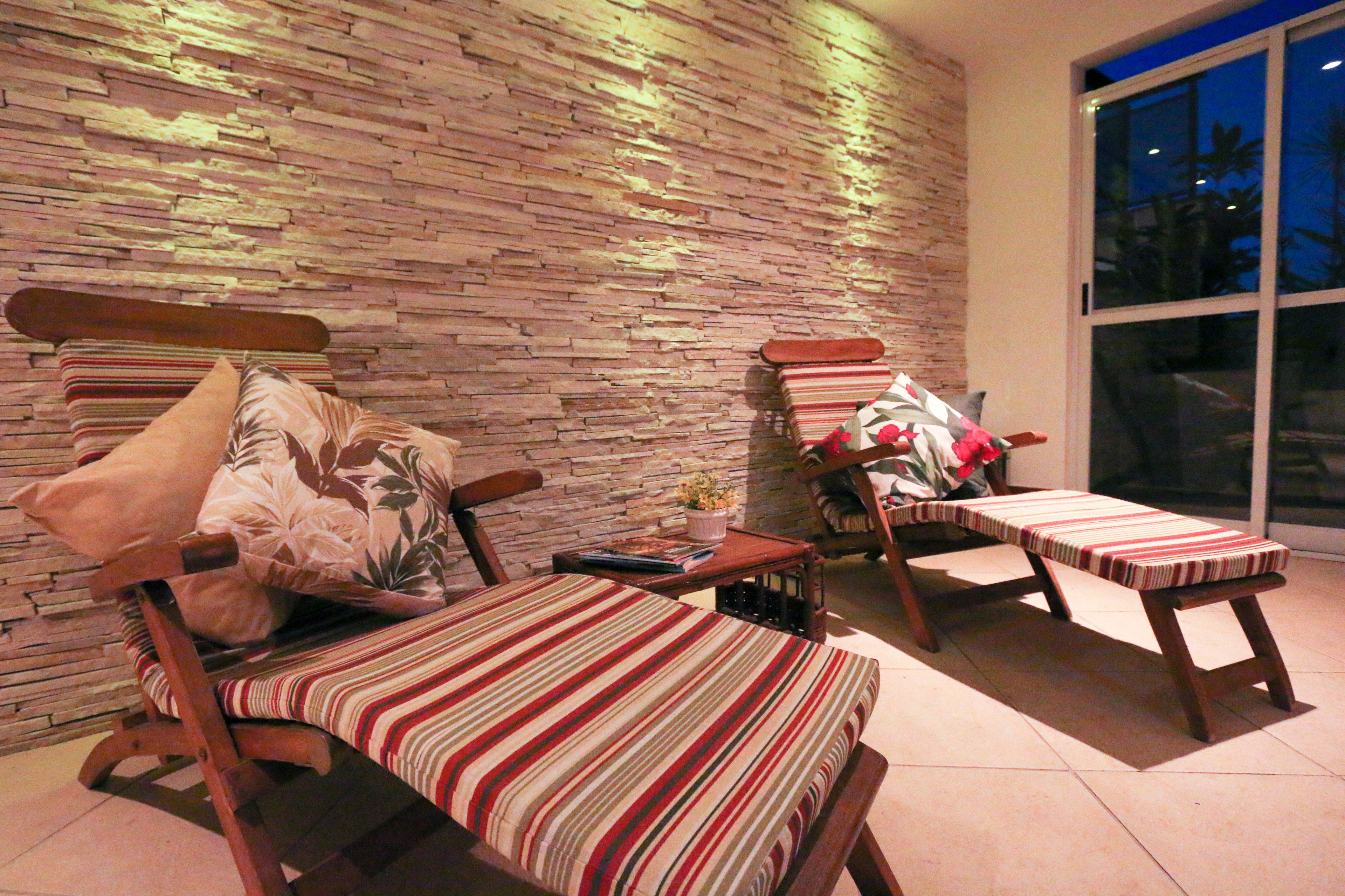 A room with a brick wall, two wooden chairs with striped cushions, and a bench.
