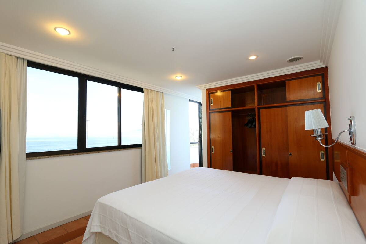 A hotel room with a large bed, a wardrobe, a window with curtains, and a ceiling light.