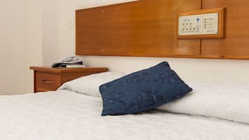 Habitación de hotel con cabecera de madera, mesita de noche con teléfono y libros, y almohada azul estampada sobre la cama.