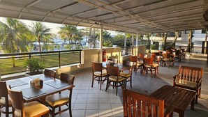 A covered outdoor seating area with tables and chairs, a fire extinguisher, and a view of palm trees and buildings. - Solar do Amanhecer (Niteroi)