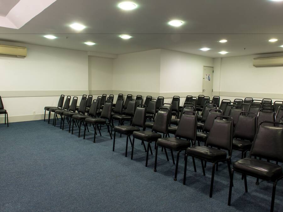 A conference room with rows of black chairs, a blue carpet, and recessed ceiling lights.