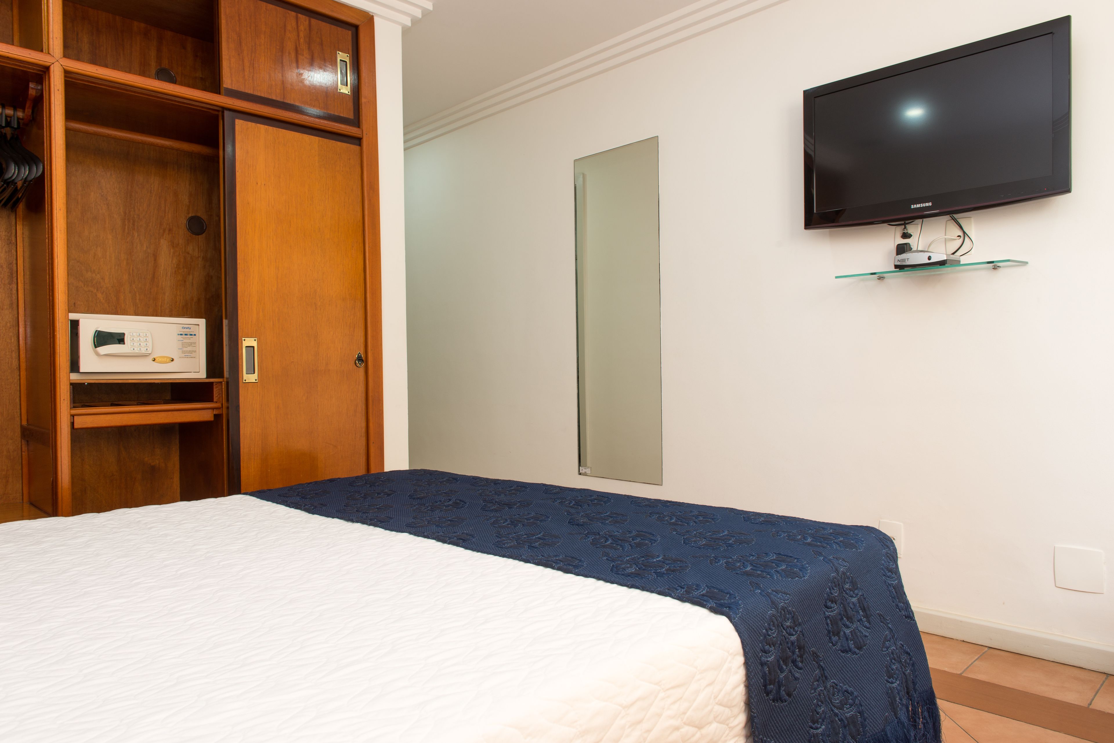 Ein Schlafzimmer mit Bett, Holzschrank, einem an der Wand befestigten Fernseher und einem Spiegel.