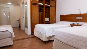 A hotel room with two beds, a wooden wardrobe, a bedside table with a lamp, and a bathroom visible through an open door.