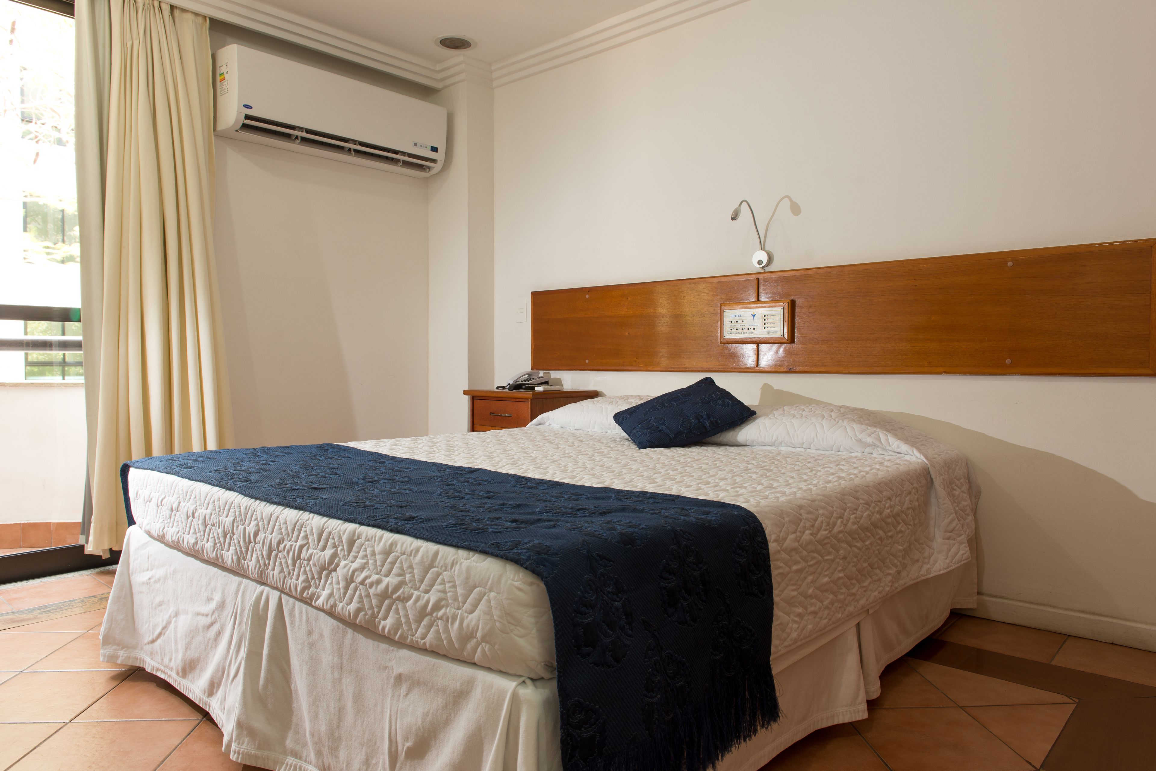 Une chambre d’hôtel équipée d’un lit, d’une table de chevet, d’une tête de lit en bois et d’un appareil de climatisation.