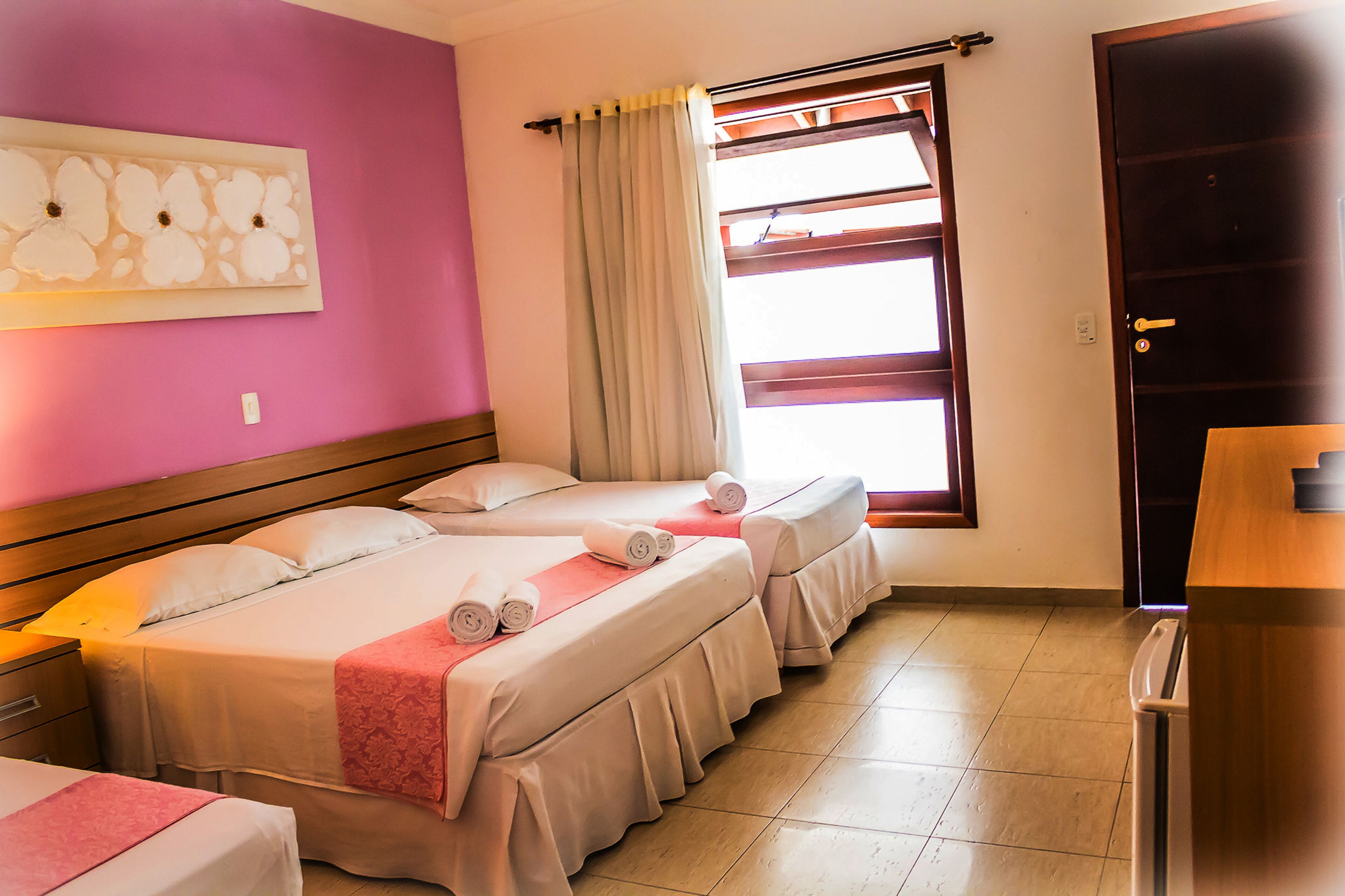A hotel room with two beds, a wooden headboard, a window with curtains, and a door.