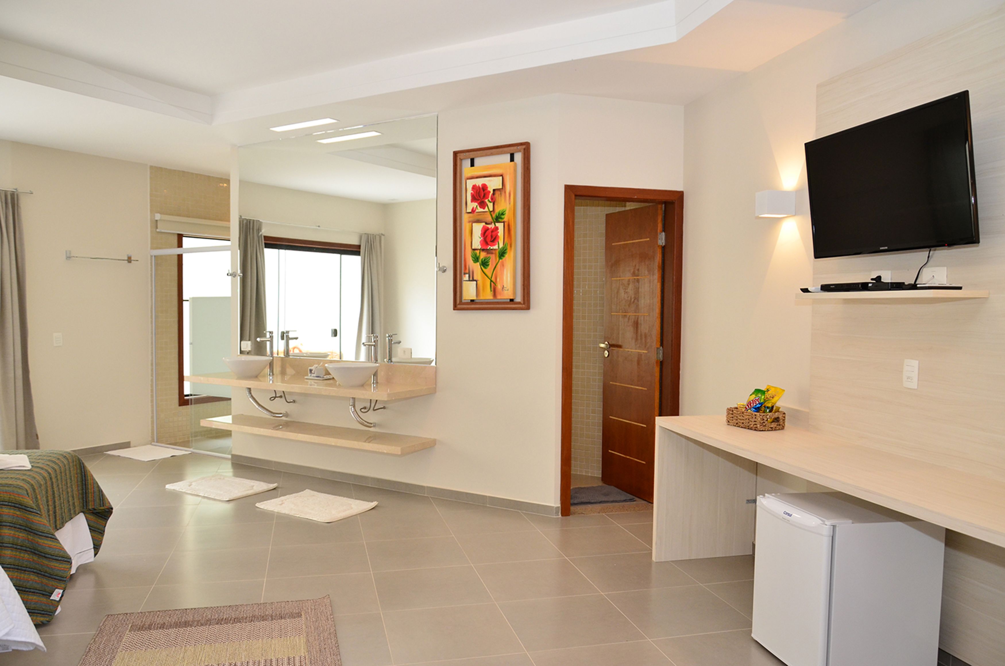 A hotel room with a bed, a bathroom with a sink and mirror, a television on the wall, and a small refrigerator.