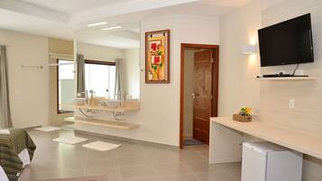 A hotel room with a bed, a bathroom with a sink and mirror, a television on the wall, and a small refrigerator.