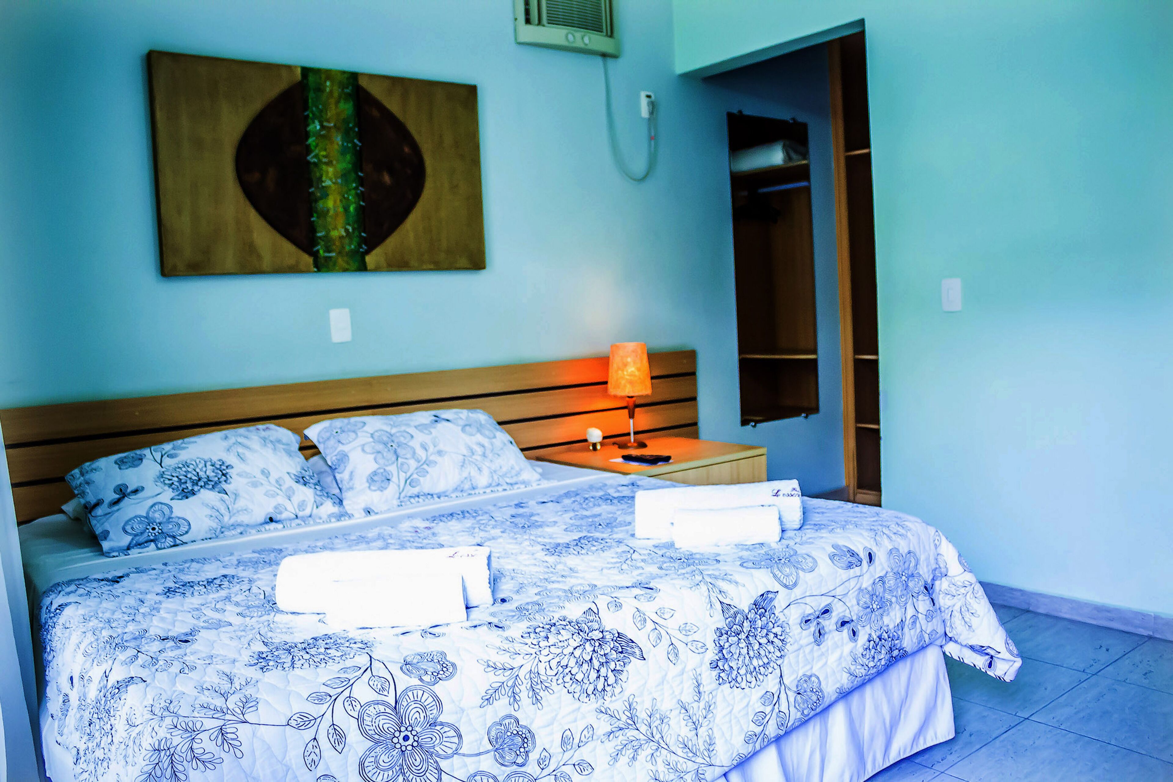 Een slaapkamer met een bed, nachtkastje, lamp, schilderij aan de muur en een inloopkast.