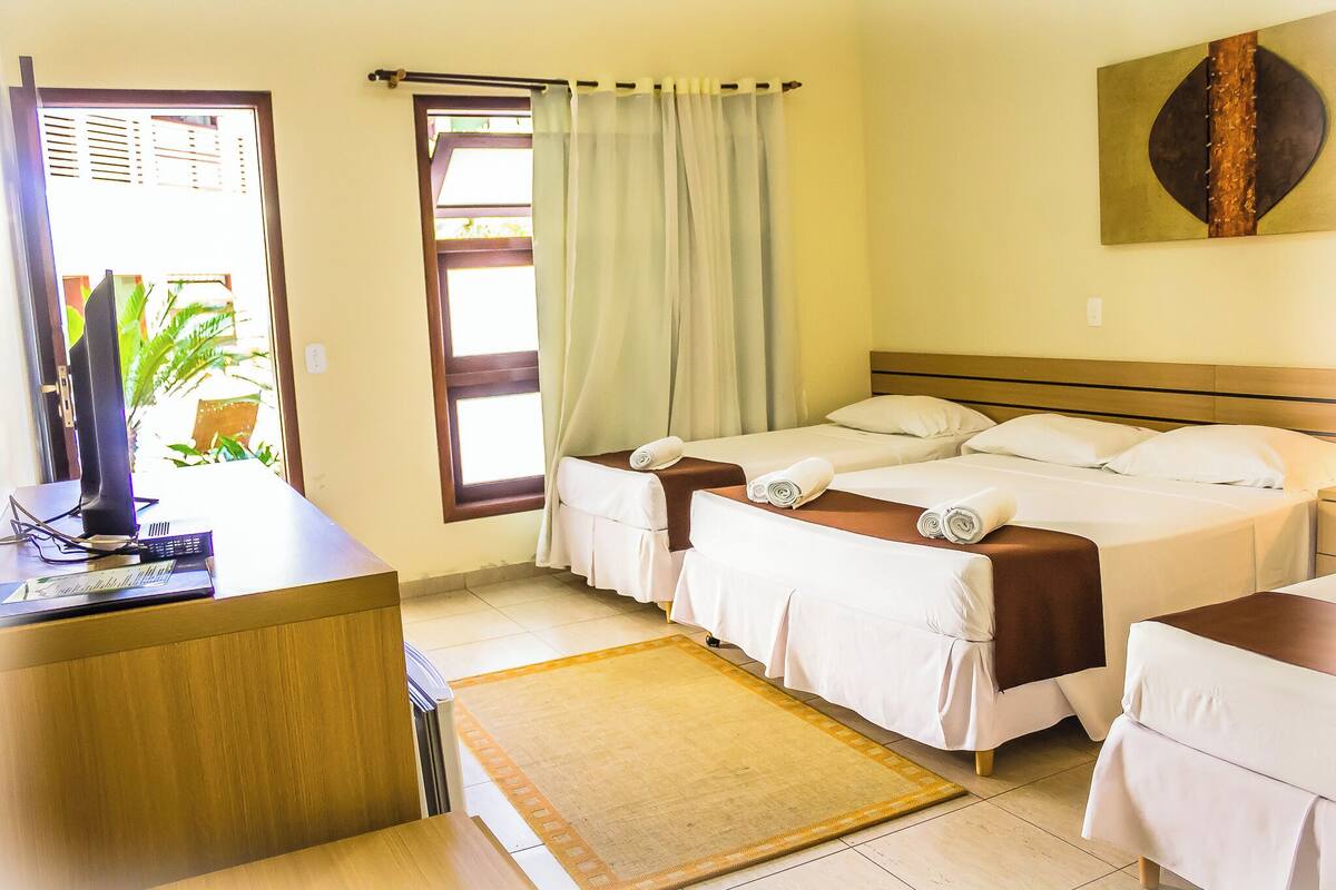 Habitación de hotel con dos camas, un escritorio, una computadora y un ventanal grande con cortinas.
