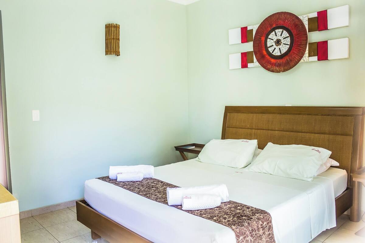 Una habitación de hotel con una cama, almohadas, una mesita de noche y un reloj de pared.