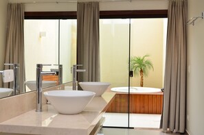 A modern bathroom with three large white sinks, a wooden bathtub, and a potted palm plant.