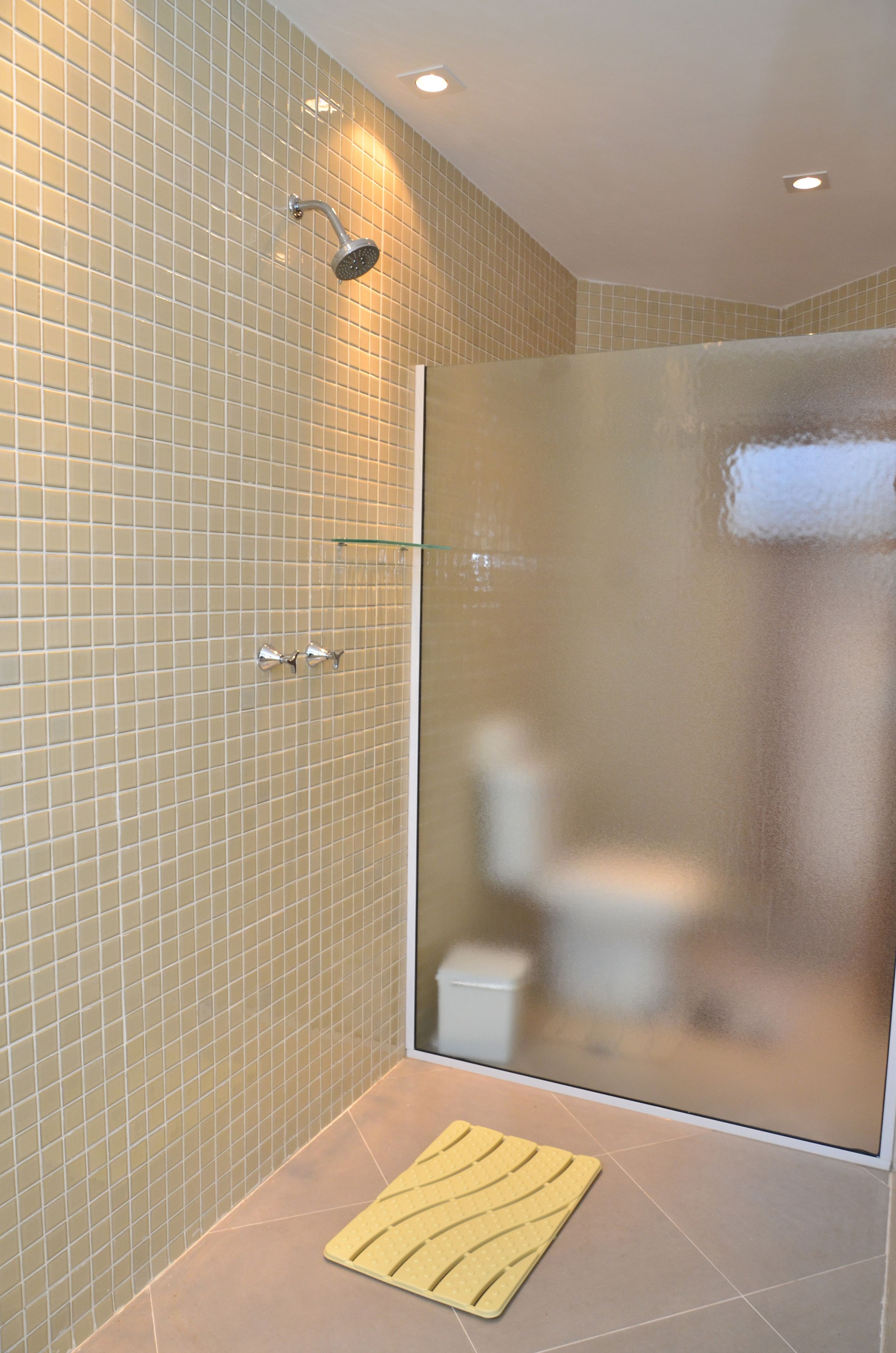A modern bathroom with a glass shower enclosure, beige tiled walls, and a glass door.