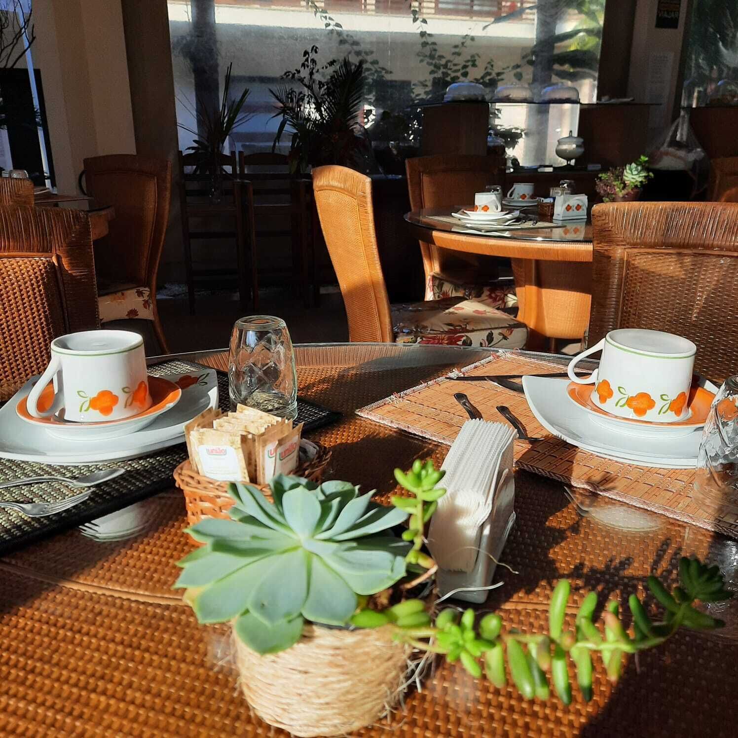 A dining table set with white plates and orange floral cups, surrounded by wicker chairs and a wicker table.