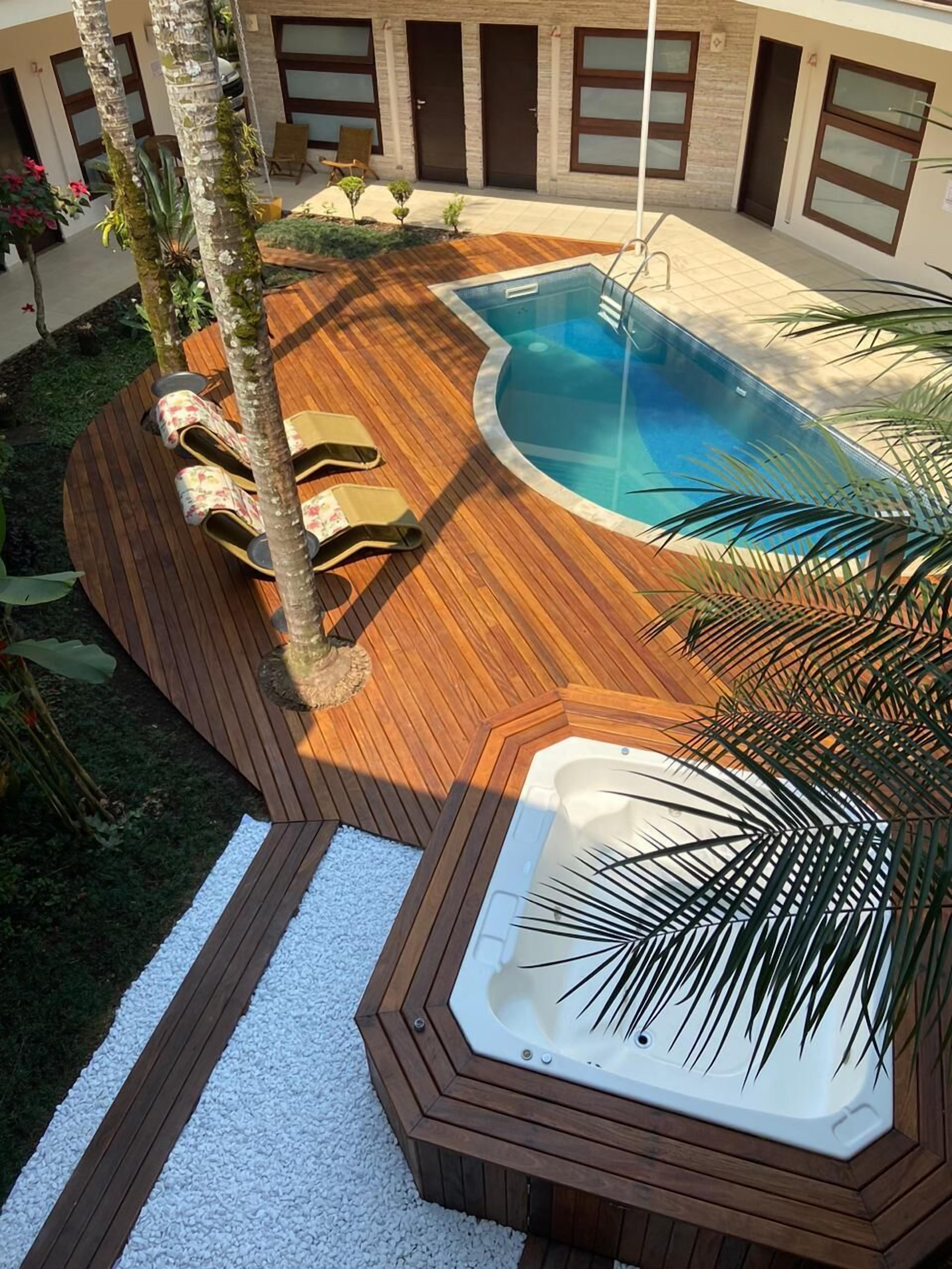 A swimming pool with a wooden deck, lounge chairs, and a hot tub.