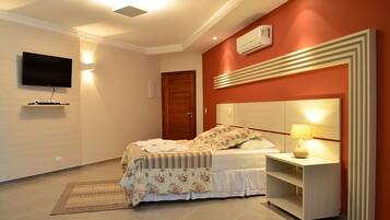 Quarto com cama, mesa de cabeceira, luminária, TV e ar-condicionado fixado na parede.