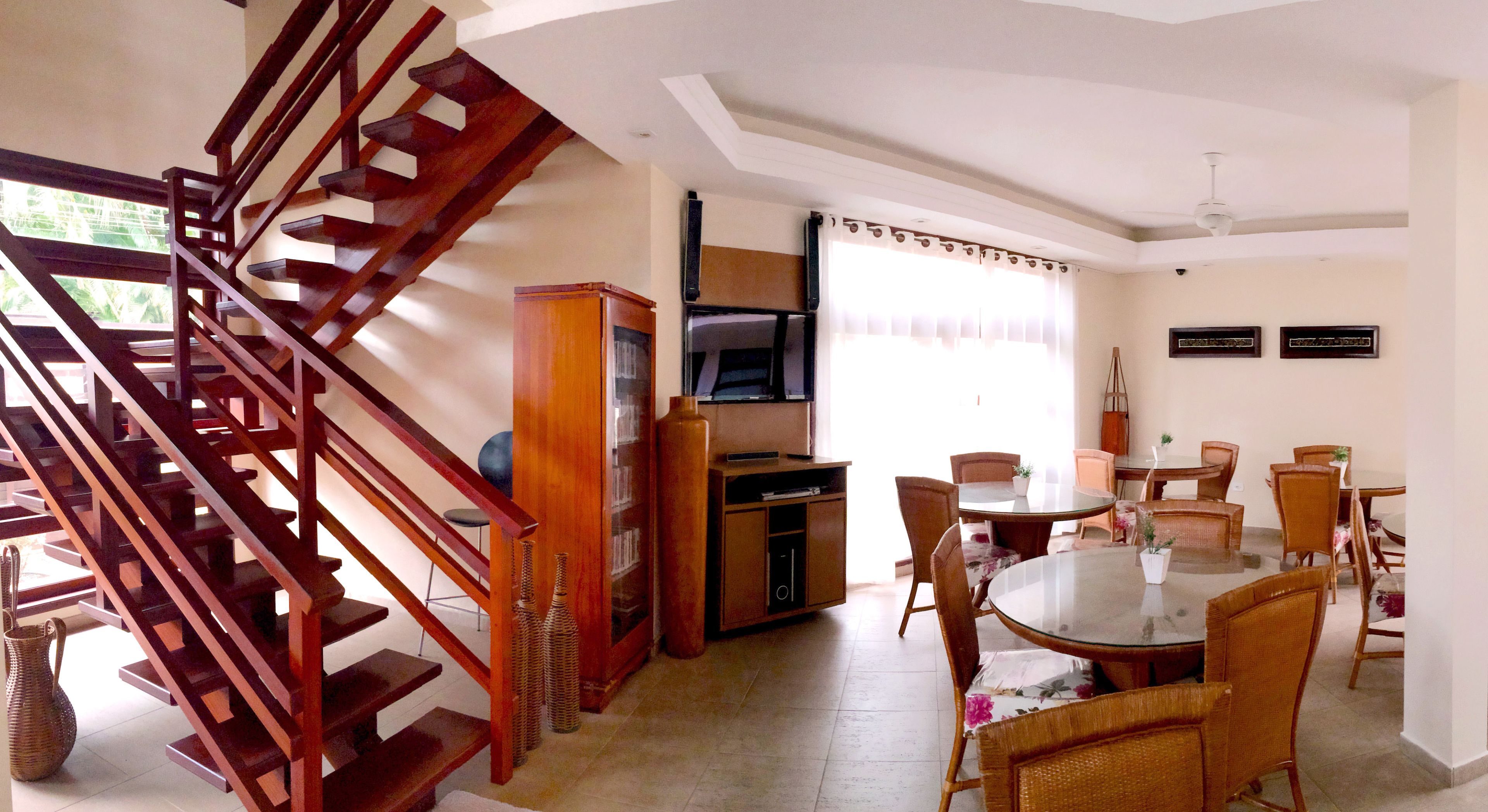A dining area with a round glass table, wicker chairs, and a wooden staircase.