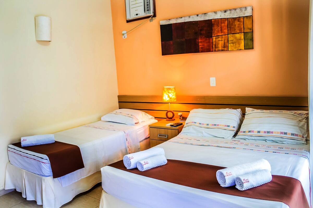 Habitación de hotel con dos camas, una mesita de noche, una lámpara y aire acondicionado instalado en la pared.