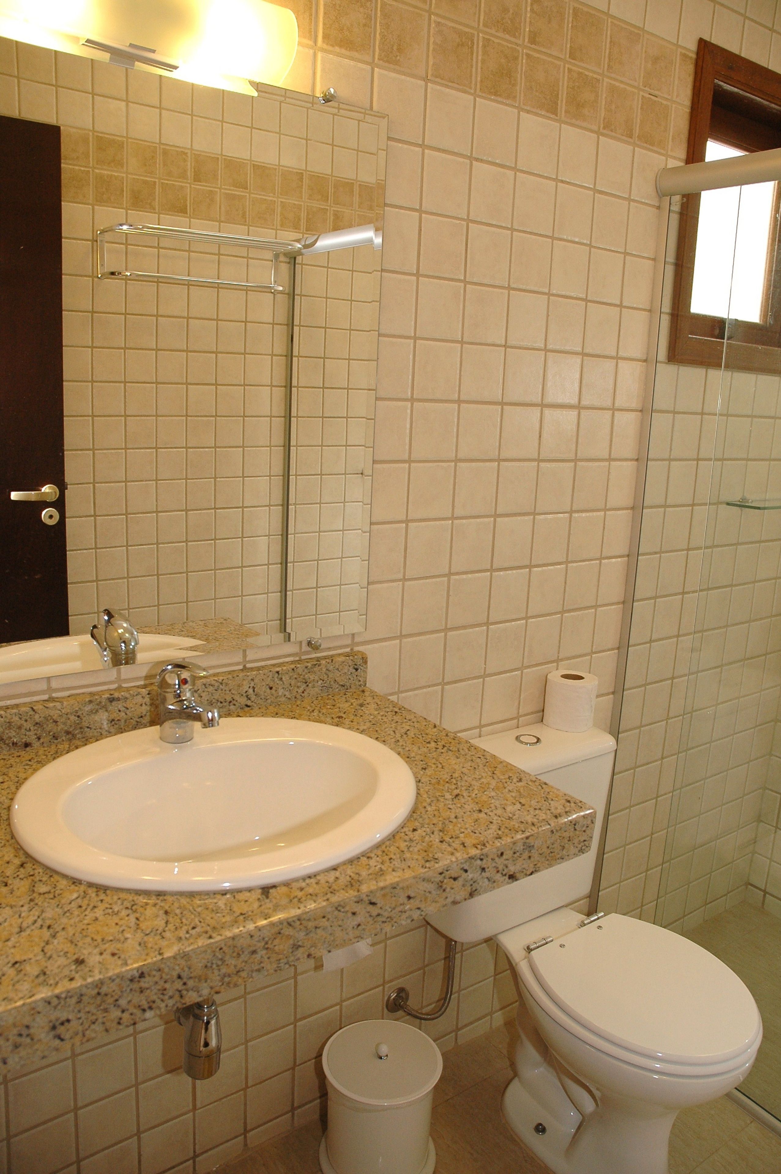 Un baño con lavamanos, espejo, inodoro y un pequeño cubo de basura.