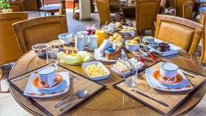Une table ronde est dressée pour le petit-déjeuner, avec divers plats disposés dessus, notamment des œufs, des viennoiseries et des boissons, et des chaises placées autour.