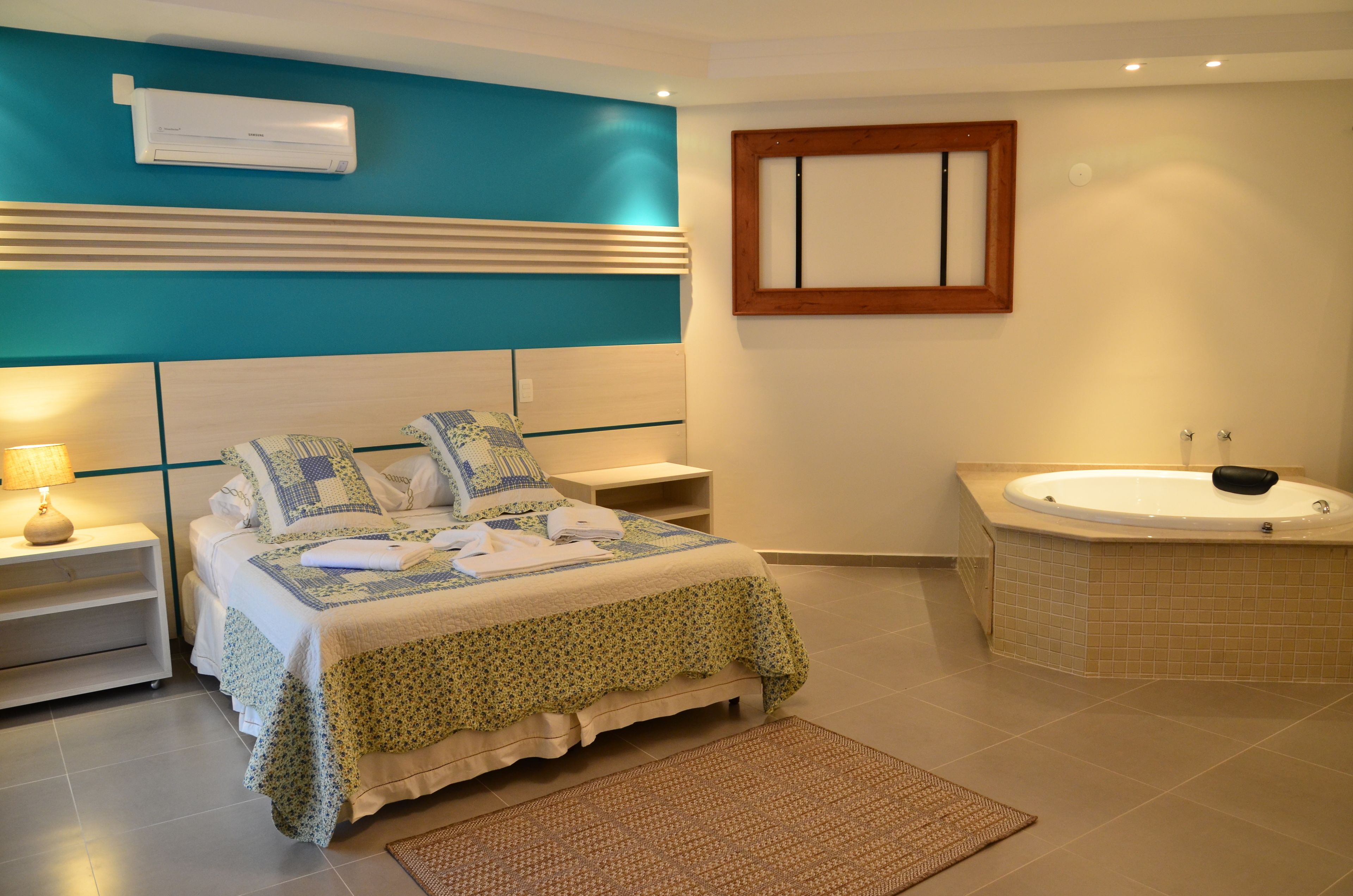 Ein Schlafzimmer mit Bett, Nachttischen, einem Badewannen-Eimer, einer Wand-Klimaanlage, einem spiegelnden Holzbettrahmen und einer Badewanne.
