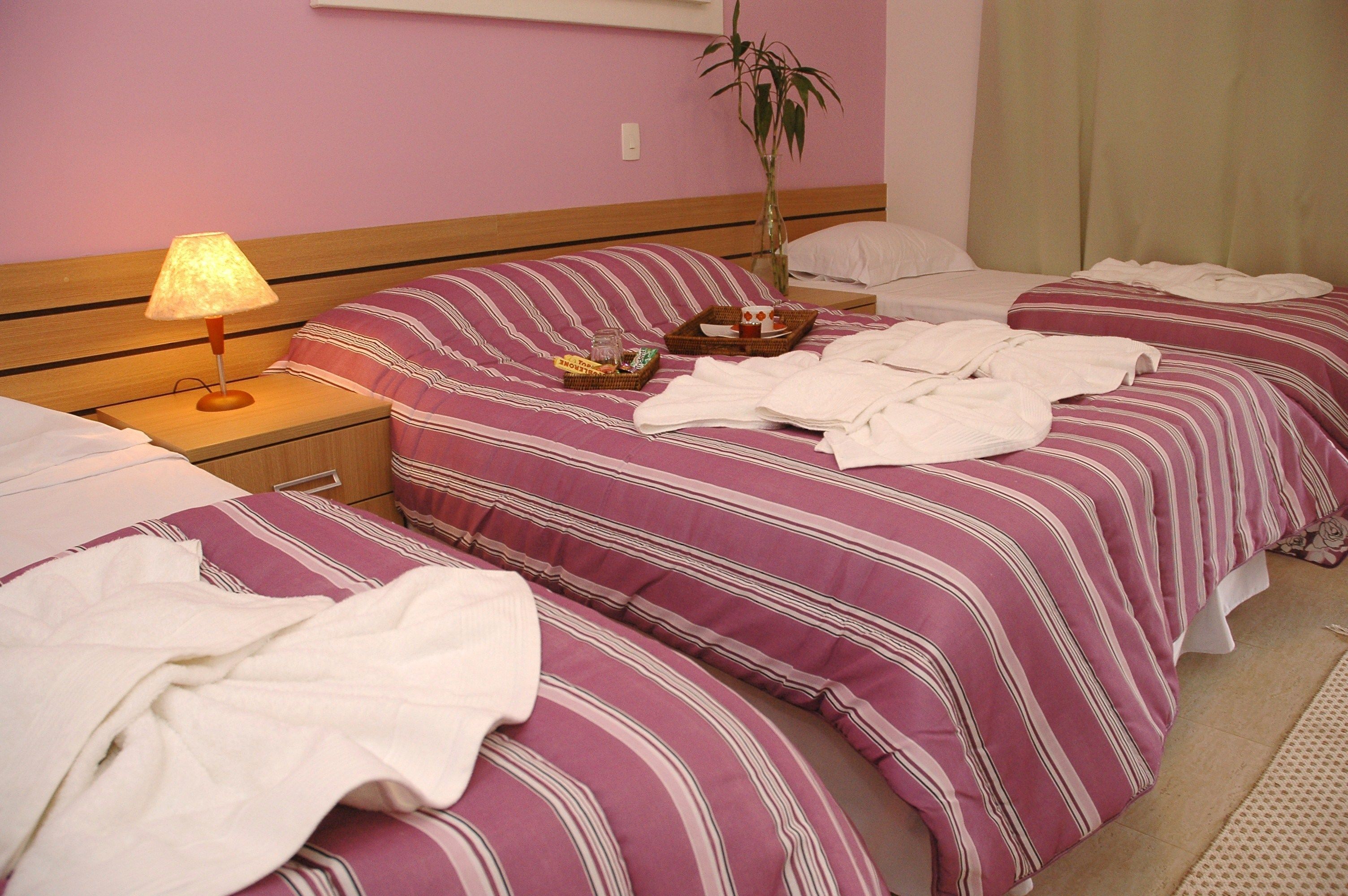 Een hotelkamer met twee bedden, een nachtkastje met een lamp, een potplant en een kleine tafel met een dienblad.