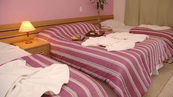 Een hotelkamer met twee bedden, een nachtkastje met een lamp, een potplant en een kleine tafel met een dienblad.