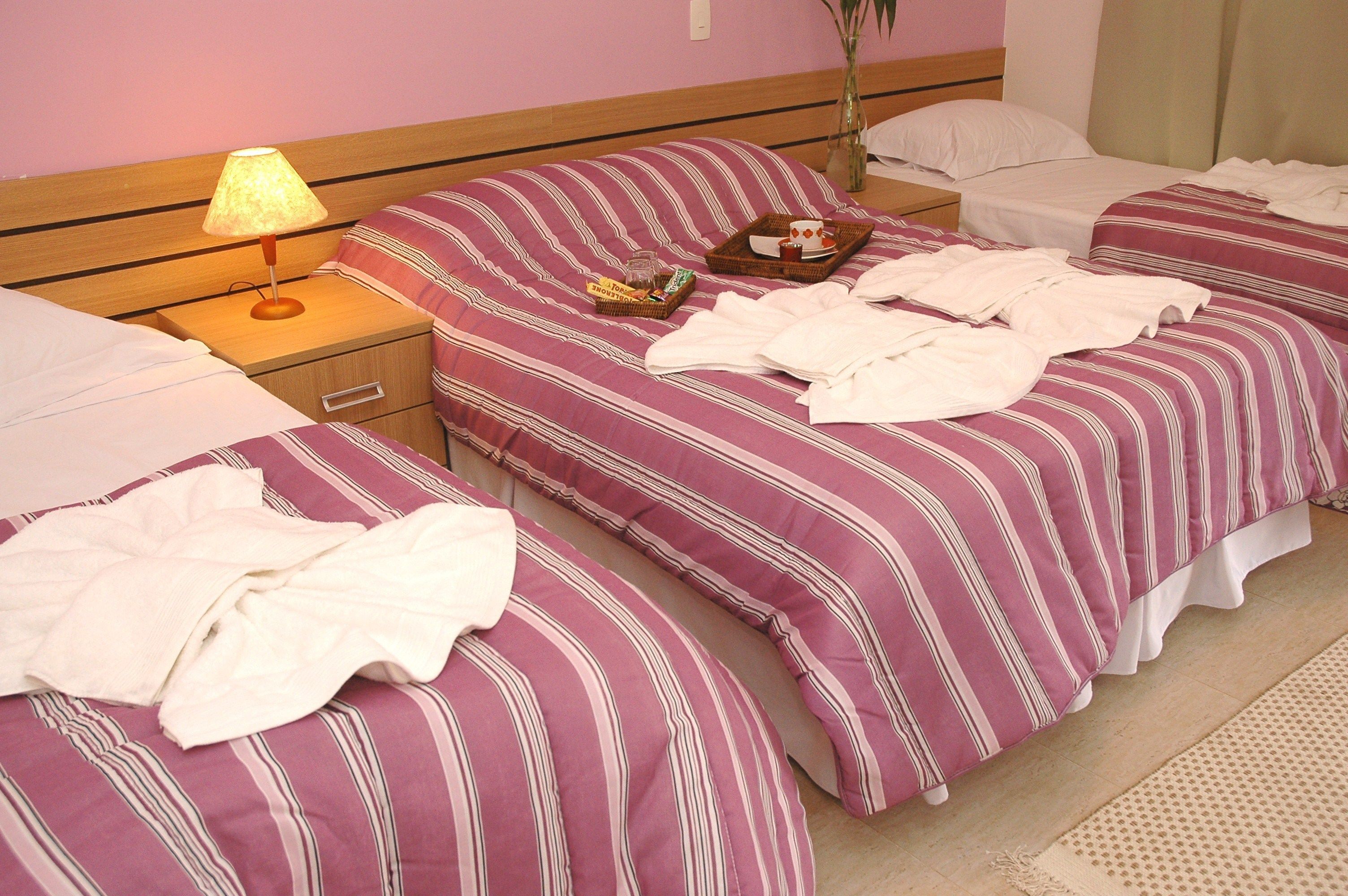 Habitación de hotel con dos camas, una mesita de noche con lámpara y una pequeña mesa con una bandeja de artículos para el desayuno.