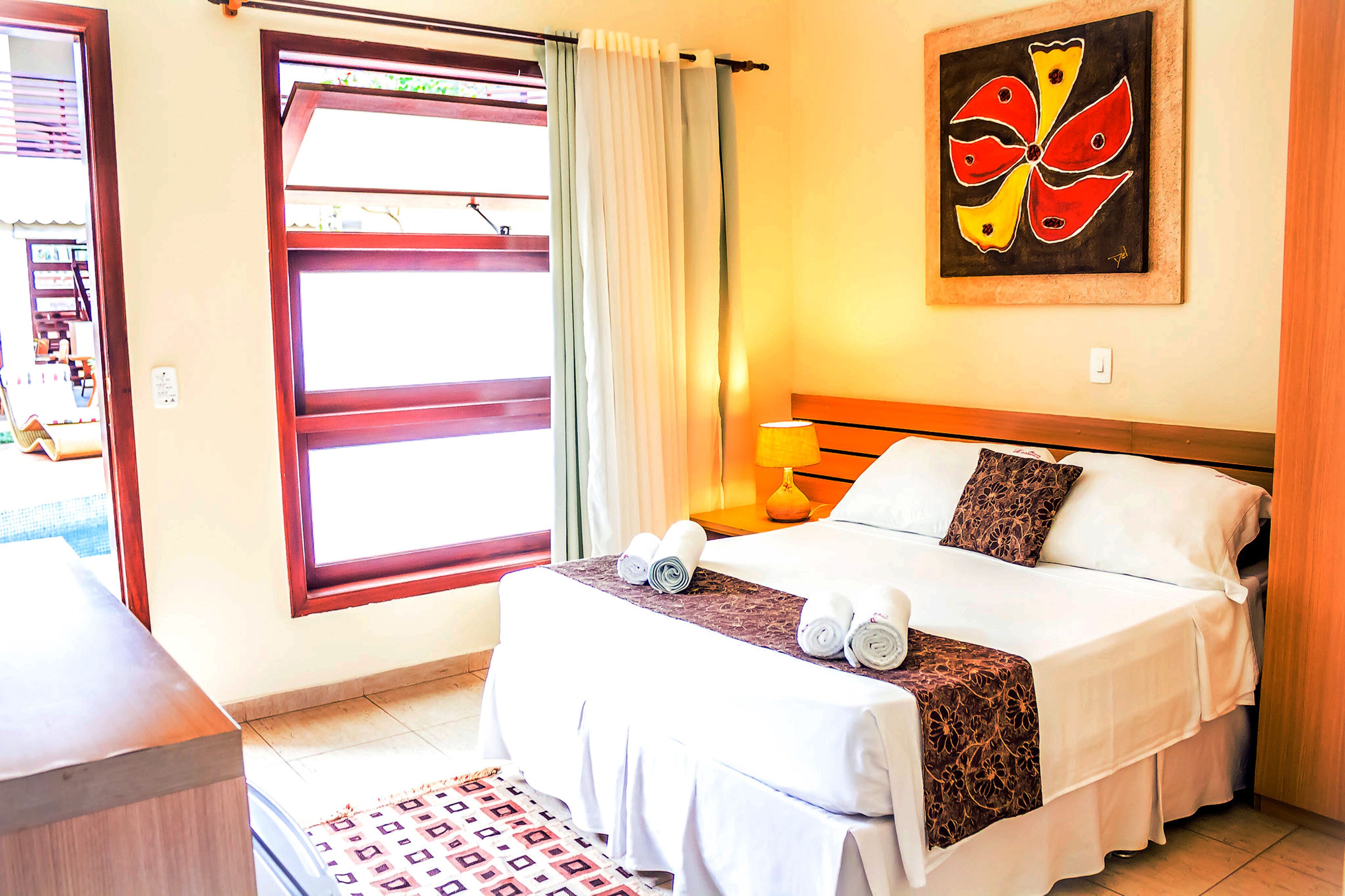 Een hotelkamer met een bed, een raam met gordijnen, een schilderij aan de muur en een lamp op het nachtkastje.