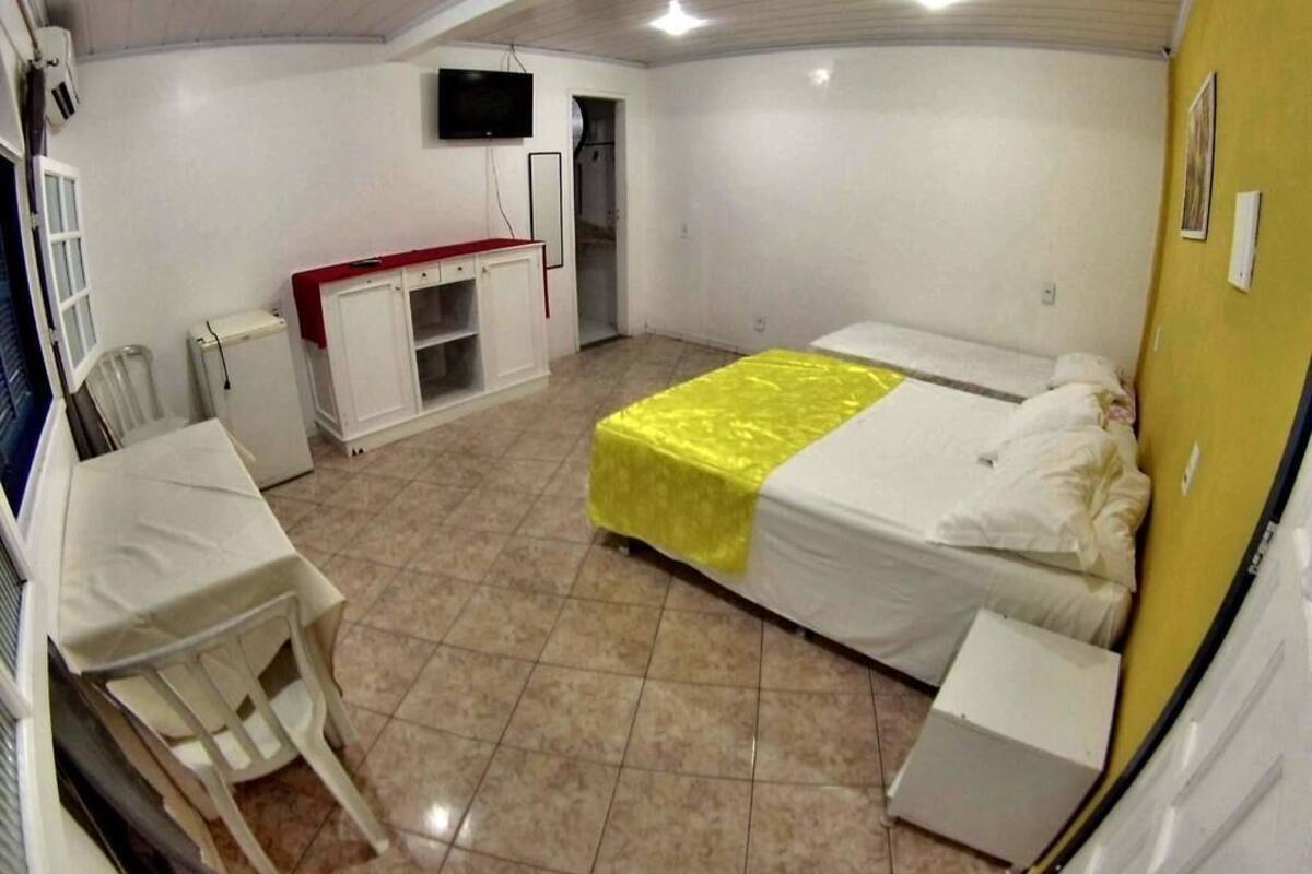 A room with a bed, a desk, a chair, a television, and a small kitchenette.