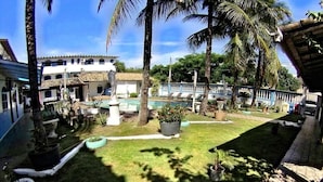 A courtyard with a swimming pool, palm trees, and a building with multiple windows. - Pousada Da Bia (RIO DAS OSTRAS)