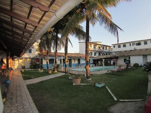 A courtyard with a swimming pool, palm trees, and a building with multiple balconies. - Pousada Da Bia (RIO DAS OSTRAS)