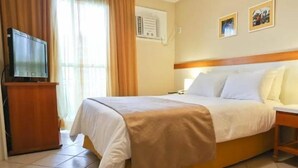 Ein Hotelzimmer mit einem Bett, einem Fernseher, einem Schreibtisch und einem Vorhangfenster.