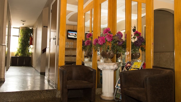 A hotel lobby with a reception desk, two armchairs, a decorative column with flowers, and a television in the background. - Hotel Puma (Rio de Janeiro)