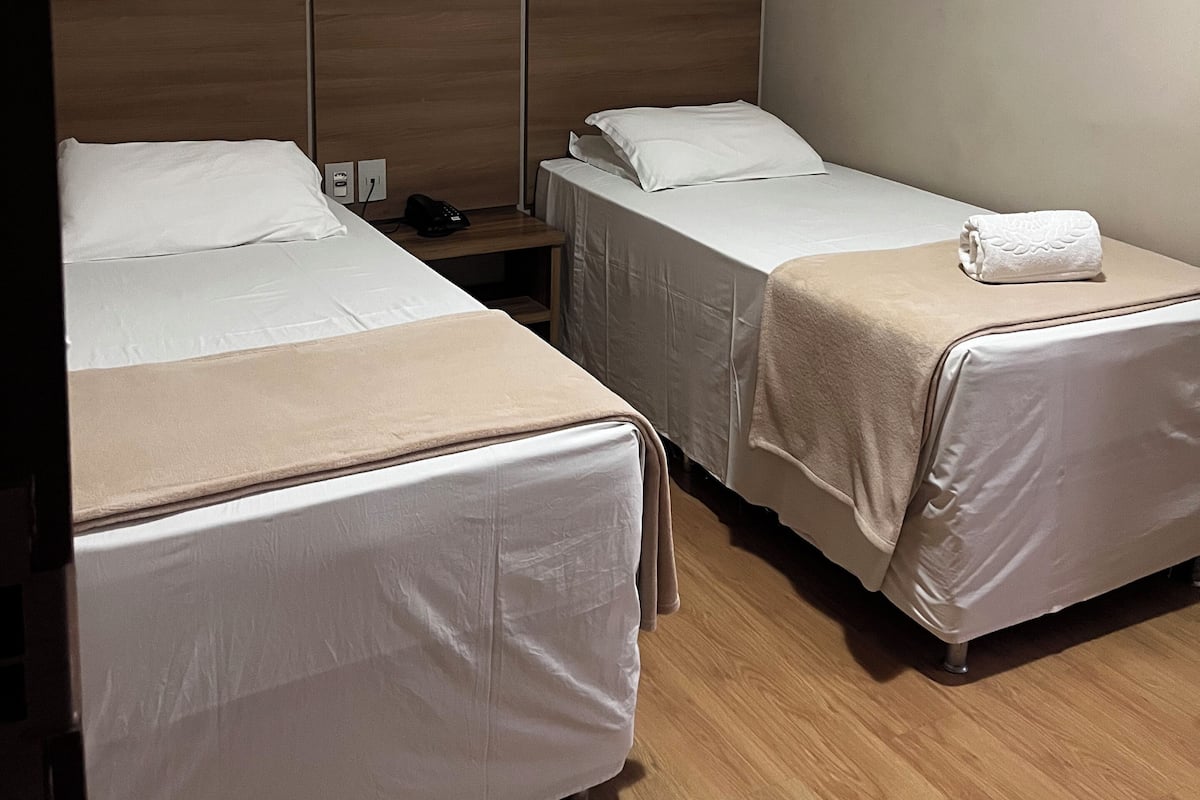 Une chambre d’hôtel avec deux lits, une table de chevet, un appareil de climatisation et un plancher en bois.