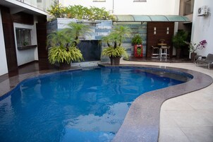 Una piscina de borde curvo, rodeada de plantas en macetas y un pequeño espacio de descanso con sillas.