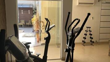 Un gimnasio en casa con dos máquinas elípticas, un juego de mancuernas y una puerta que da a un patio con mobiliario exterior.