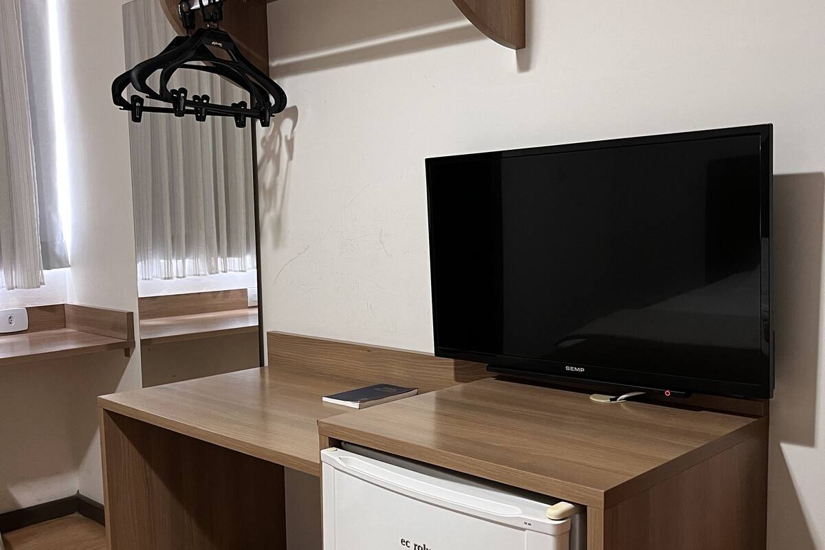 Un espace de vie compact comprenant un bureau en bois, un téléviseur à écran plat et un petit réfrigérateur.