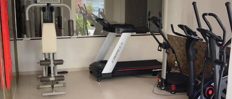 A gym with a treadmill, elliptical, and weight machine.
