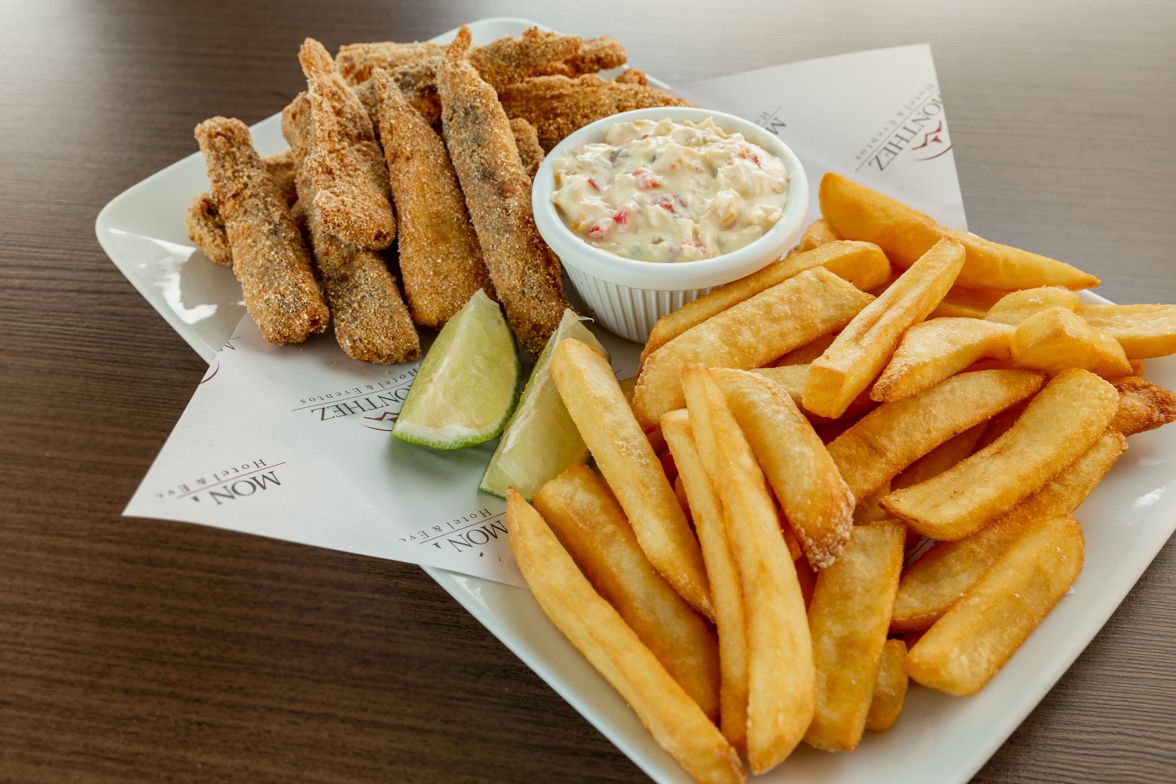 Um prato com palitos de peixe empanados, batatas fritas e um molho com gomos de limão.