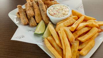 Um prato com palitos de peixe empanados, batatas fritas e um molho com gomos de limão.